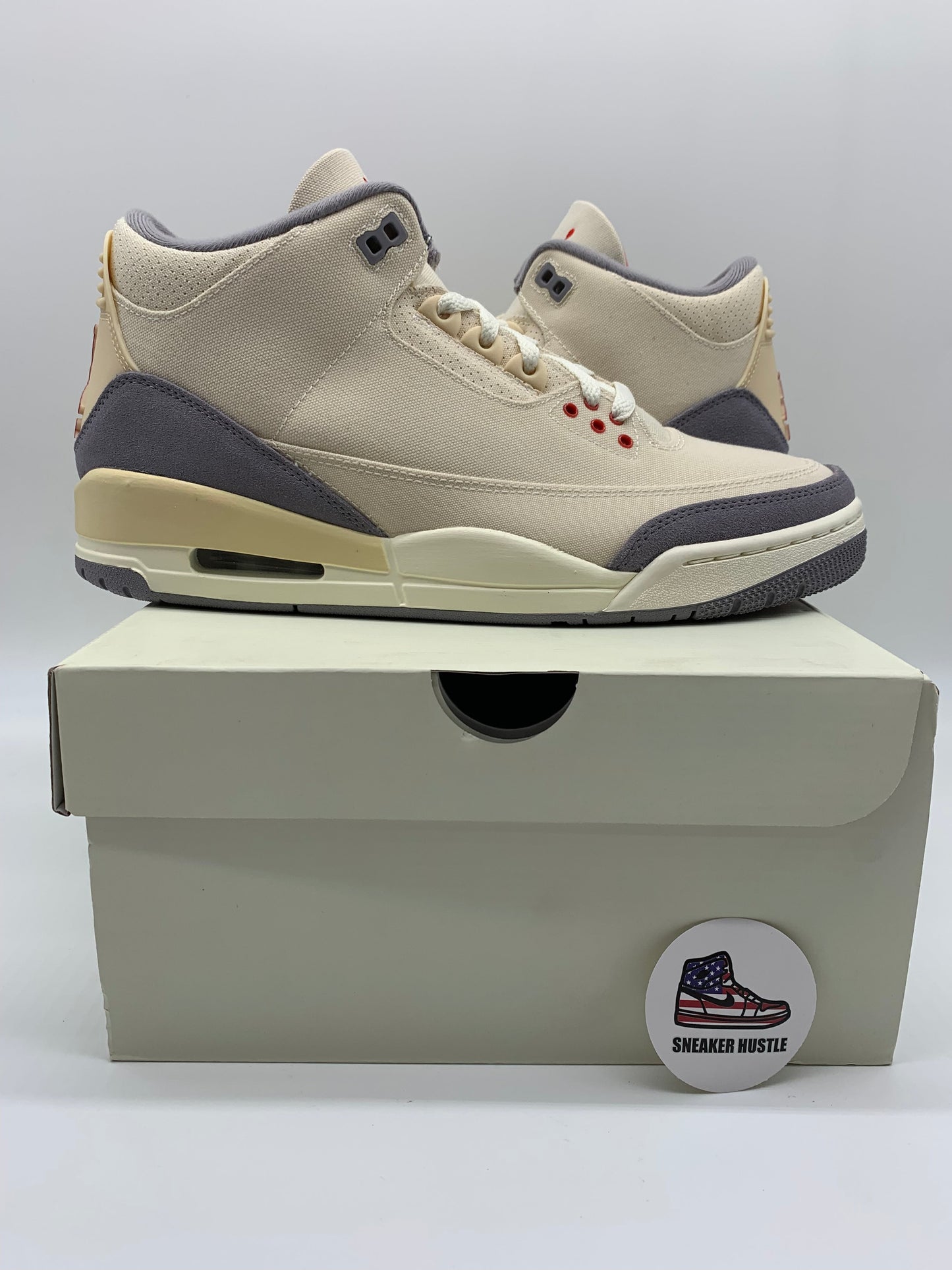 Jordan 3 Retro Muslin sneakers in cream and grey colorway displayed on a shoebox with Sneaker Hustle logo badge